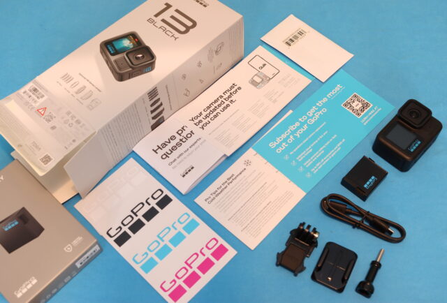 Unboxing a brand new GoPro Hero 13 Black camera with accessories on a wooden desk.