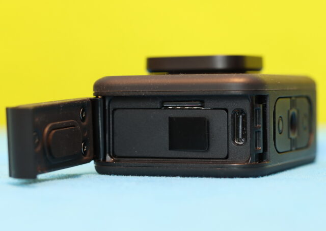Close-up of GoPro Hero 13 Black battery compartment with the door open, showing the rubber waterproof seal, microSD card slot, and USB-C charging port.