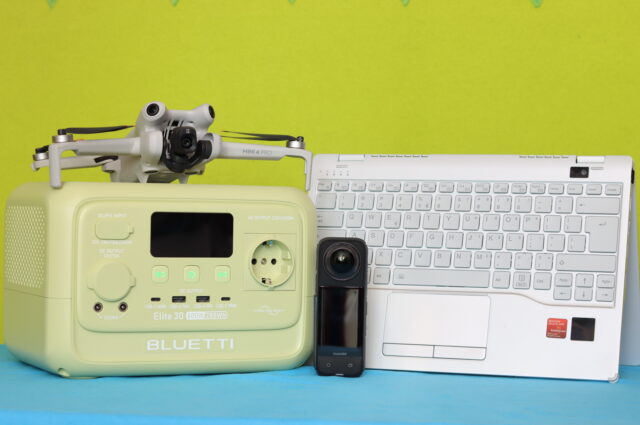 A 600W portable power station simultaneously powering an action camera, a drone battery charger, and a laptop