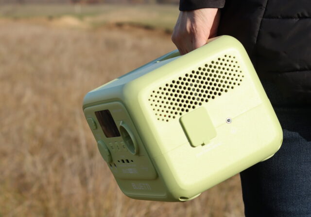 Person carrying the Bluetti Elite 30 V2 power station with one hand while walking into a forest.