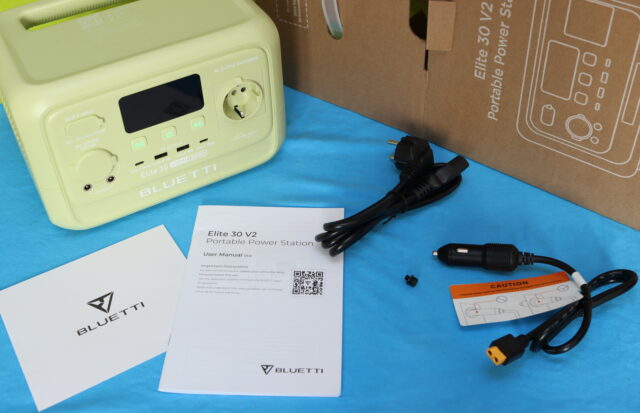 Unboxing the Bluetti Elite 30 V2 power station, with the device displayed on a table alongside the included charging and connection cables arranged neatly.