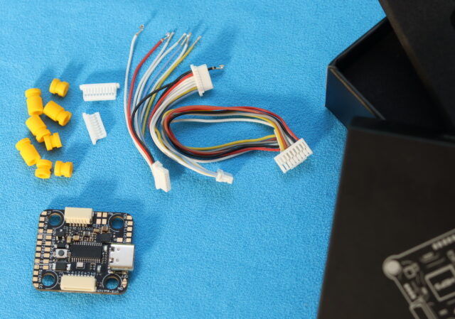 Unboxing the MEPS AeroCore F7 Mini Flight Controller showing the board, wiring, and accessories on a table.