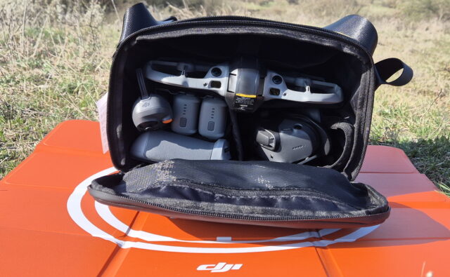 Photo of the DJI Avata 360 shoulder bag showing how the drone, RC 2 controller, Motion Controller 3, Goggles, three batteries, charger, and landing pad are loaded and organized inside.