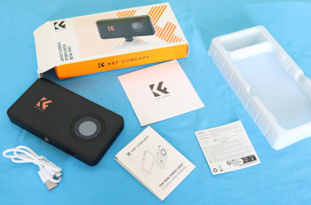 Unboxing the K&F Concept RGB video light showing the compact LED panel, accessories, and packaging contents laid out on a table