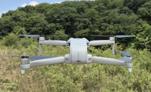 Rear view of the Ruko F11PRO 2 Plus drone in mid-air flight over an open landscape, showing stable hovering and smooth GPS-assisted positioning from behind.