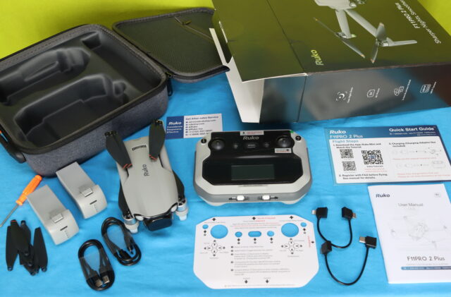 Ruko F11PRO 2 Plus unboxing showing the drone, remote controller, intelligent flight battery, charger, spare propellers, cables, and user manual neatly arranged on a table.